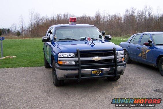 Blue Chevrolet Tahoe police SUV with a push bar and light bar, parked next to a blue Ford Crown Victoria