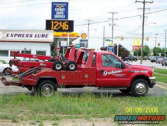 Red tow truck with Graham's Crossroads Towing logo and phone number. Gas station and McDonald's in background