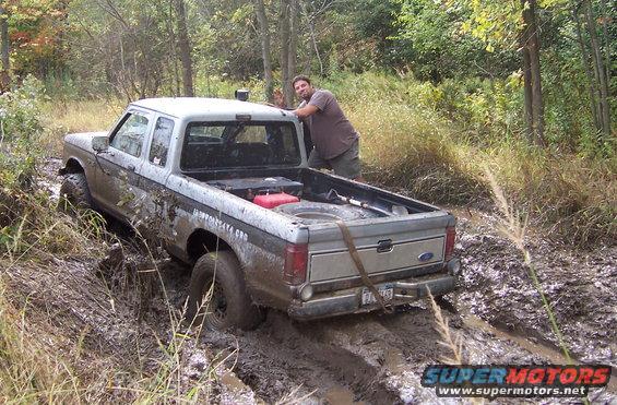 Silver Ford pickup truck stuck in mud with a man leaning on the tailgate