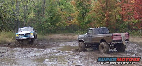Brown pickup truck with red tailgate and a blue truck in mud