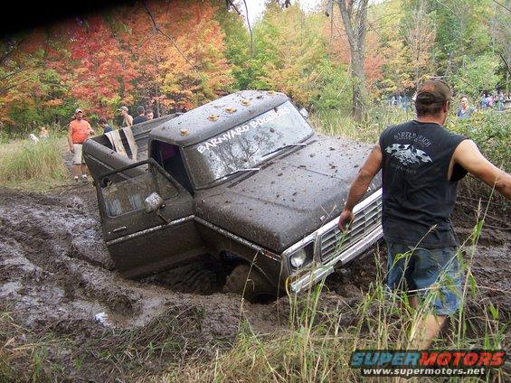 SUV stuck in mud, person trying to push it out