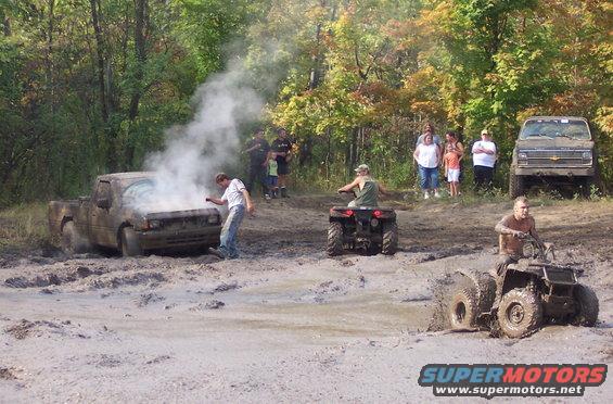 Muddy truck with smoke from hood, people watching, ATVs in mud