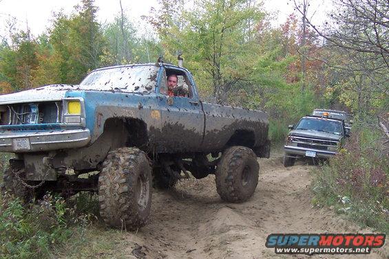 Muddy lifted pickup truck driving on a dirt trail with another truck behind it
