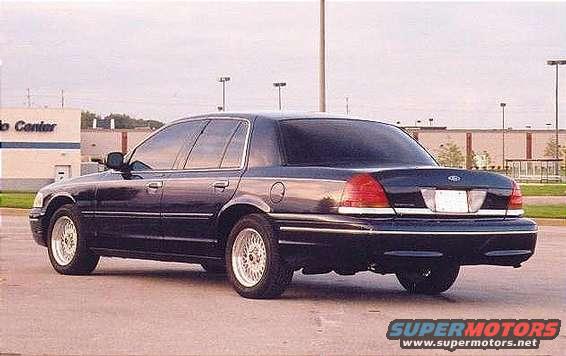 Dark sedan, rear 3/4 view, parked on asphalt. Building in background
