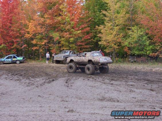Mud-covered monster truck with large tires, viewed from the rear-right