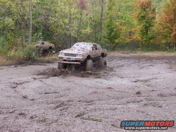 Mud-splattered lifted truck navigating a muddy track with another vehicle in the background