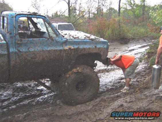 Mud-covered blue pickup truck with a person bending over its front bumper