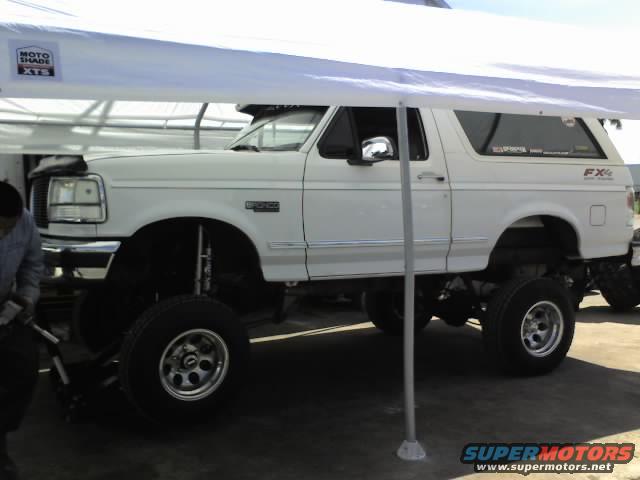 Lifted white 1995 Ford Bronco parked under a white canopy