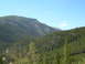1996 Jeep Cherokee - A vast mountain scene unfolds with a winding road cutting through a dense forest under a bright blue sky.