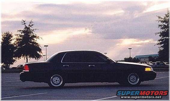 Dark sedan parked in a lot, side view, cloudy sky