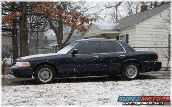 Dark sedan parked on snowy ground, house in background