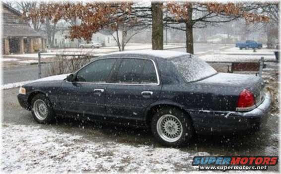 Dark sedan parked on a snowy street, trees with bare branches overhead