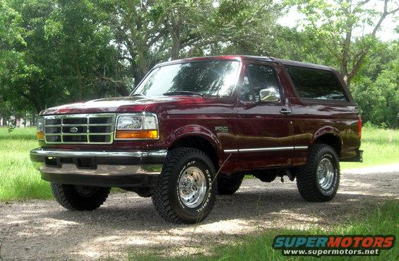 Red 1996 Ford Bronco parked on a dirt road with trees in the background