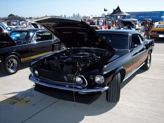 Black 1969 Ford Mustang Mach 1 with hood open, parked next to another Mustang