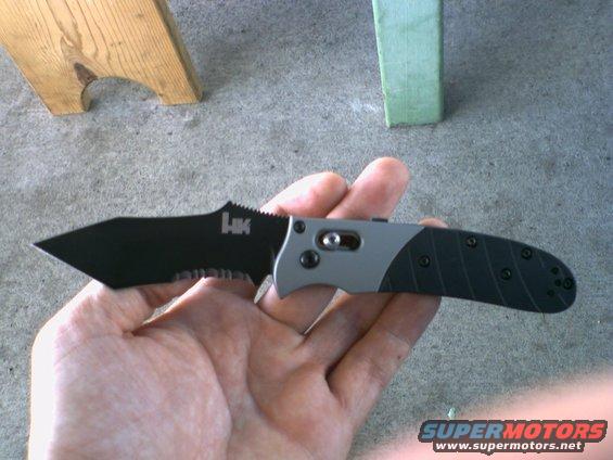 Folding knife with black serrated blade and gray/black handle held in hand