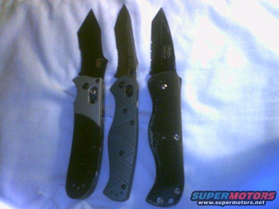 Three folding knives laid out on a blue cloth. One has a grey and black handle, one is dark grey, and the third is black