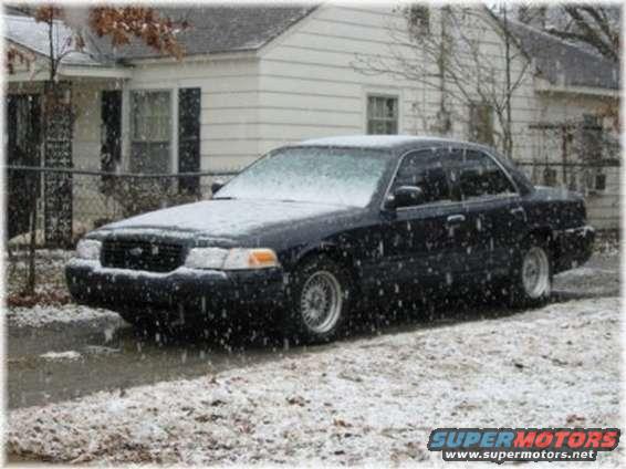 Black Ford Crown Victoria parked in front of a house during snowfall