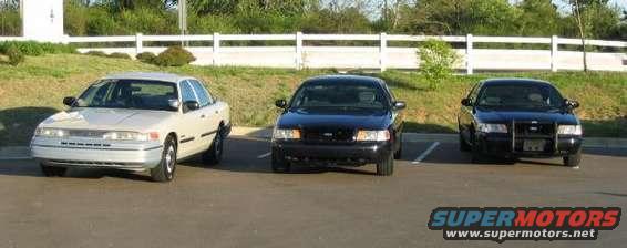 Three Ford Crown Victorias parked in a lot; one light-colored sedan in front, two dark sedans behind