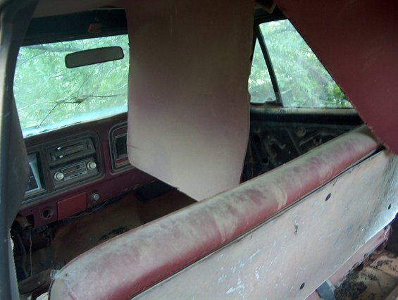 Interior view of an old vehicle, showing dusty red seats, dashboard with radio, and cracked windshield