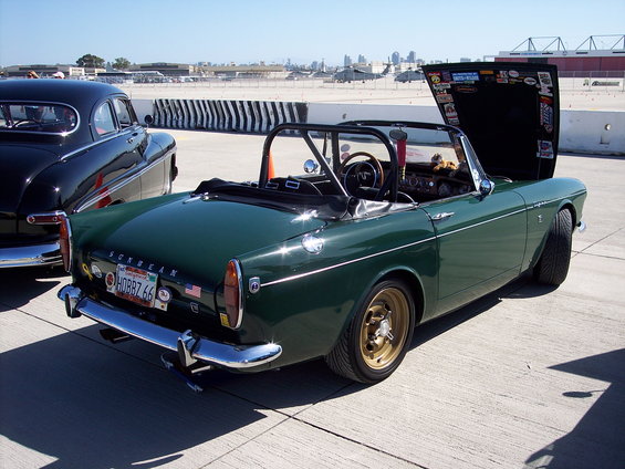 Green convertible sports car with gold wheels and a roll bar, hood open, parked next to a black car