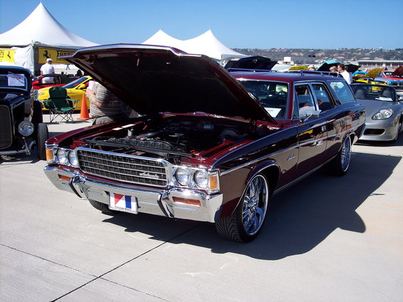 Maroon station wagon with hood open, showing engine. Chrome wheels, custom rims. Other cars and tents in background