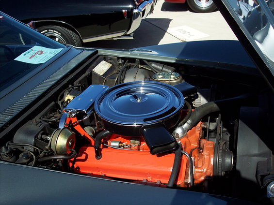 Engine bay with chrome air cleaner and orange engine block. Another car is visible in the background