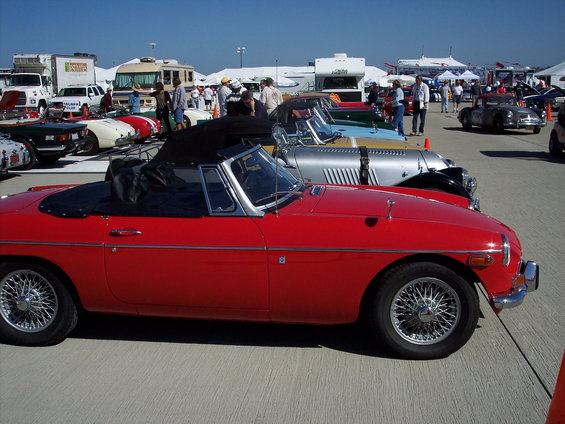Red convertible sports car parked in a line with other vintage cars and RVs