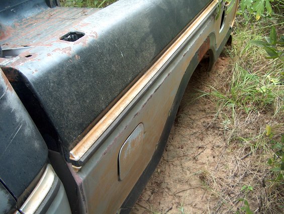 Side view of a rusty 1979 Ford Bronco's rear fender and tailgate area