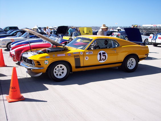 Yellow 1970 Ford Mustang Boss 302 race car with number 15 on door, hood open, parked on pavement