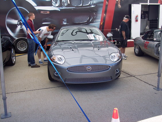 Gray Jaguar XK parked with a blue ribbon in front. Another car with number 62 visible to the right