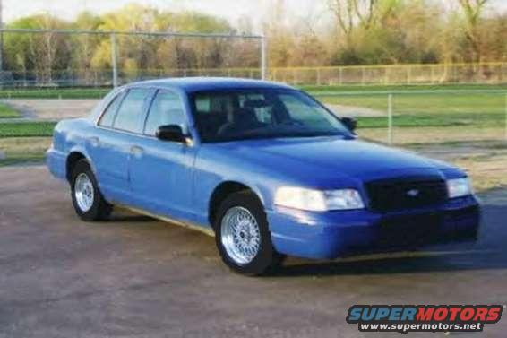 Blue sedan parked on pavement, fence and trees in background
