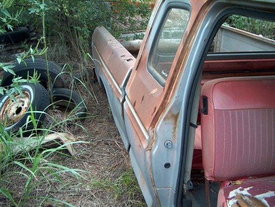 side view of rusty pickup truck cab with red seats, parked in weeds