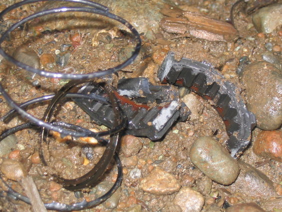 Broken black rubber belt with metal reinforcement, lying on wet ground with rocks and debris