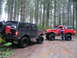 1989 Ford Bronco - Two modified Ford Broncos navigate a muddy forest trail, one black and one red, with large off-road tires.