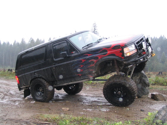 Black Ford Bronco with red flames on hood, lifted with big tires, driving over rocks off-road