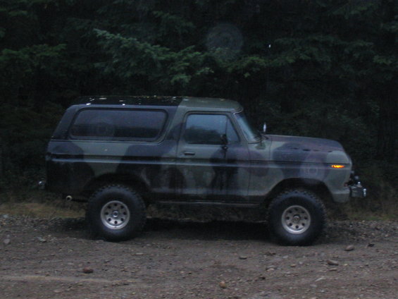 Side view of a camouflaged 1989 Ford Bronco parked on a dirt road