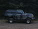 1989 Ford Bronco - This 1989 Ford Bronco, seen in a side profile, is painted in a camouflage pattern and parked on a gravelly surface with trees in the backgr…