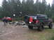 1989 Ford Bronco - Two off-road vehicles are parked in a wooded area with rocks scattered around.