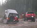 1989 Ford Bronco - Two modified Broncos navigate a wet, wooded trail with one vehicle partially on a log.