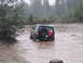 1989 Ford Bronco - A black 1989 Ford Bronco navigates through a muddy water crossing in a wooded area.