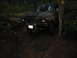 1989 Ford Bronco - A dark-colored SUV is seen on a muddy forest trail, partially obscured by trees.