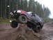 1989 Ford Bronco - A modified black Ford Bronco with flame decals navigates an off-road obstacle on a muddy trail.