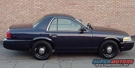 Dark blue sedan parked in front of a brick wall. It has steel wheels and a police-style light on the driver's side mirror