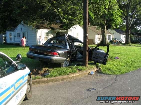 Black sedan crashed into a pole, roof crushed, doors open, front police car visible