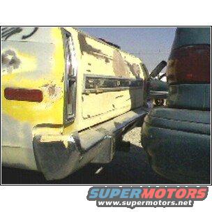 Rear corner of a beat-up yellow car, looks like it's in a junkyard