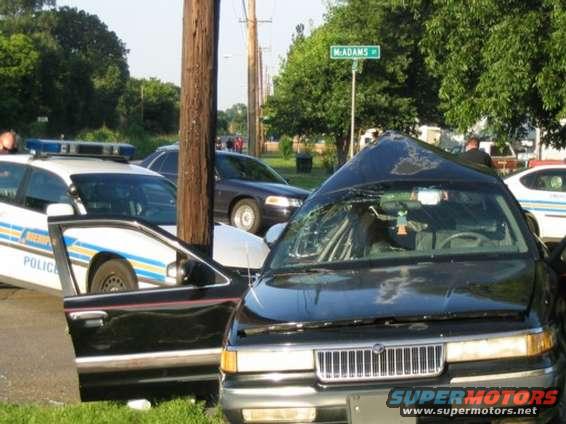 Damaged black sedan, police car, and another sedan at an intersection with a street sign that says McAdams