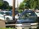 1999 Ford Crown Victoria - A black sedan with a heavily damaged roof sits at an intersection next to a police car.