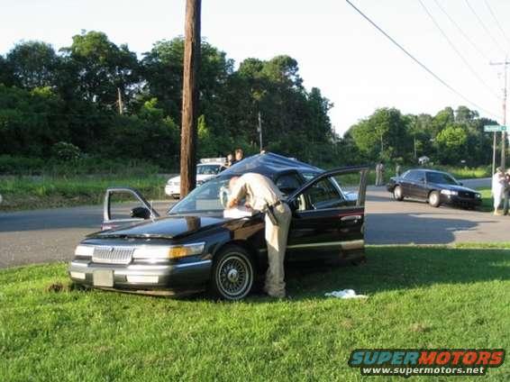 1999 Ford Crown Victoria, black, 3q-front view, person in uniform examining hood