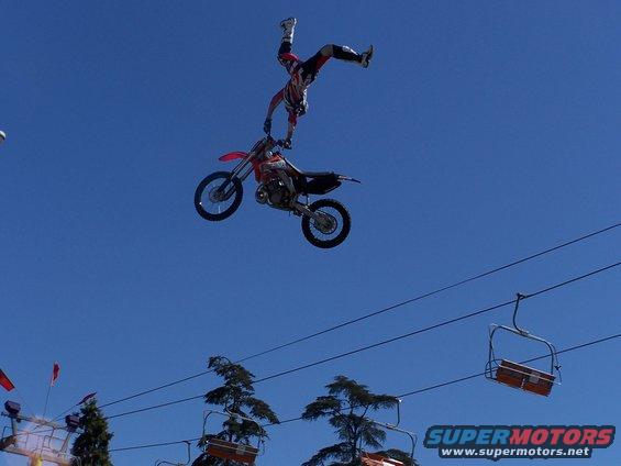 Dirt bike stunt rider in mid-air, side view. Supermotors.net logo visible