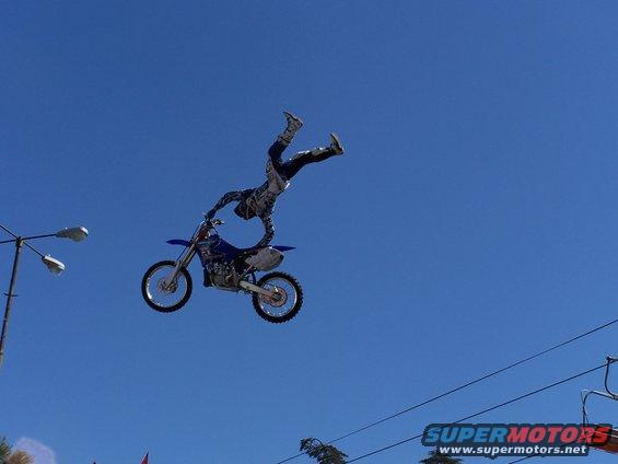 Motocross rider mid-air on a dirt bike, performing a stunt against a clear blue sky